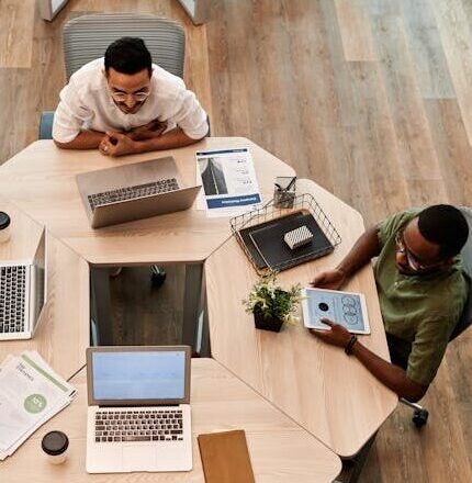 Top view of diverse team engaged in discussion with laptops and digital devices in modern office setting.