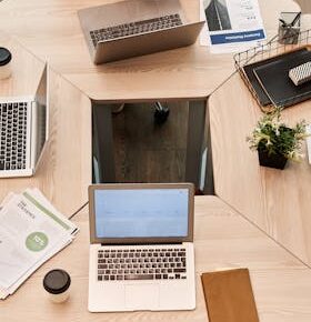 Top view of diverse team engaged in discussion with laptops and digital devices in modern office setting.