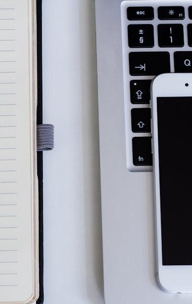 Close-up of a notebook, pen, smartphone, and laptop on a modern workspace.
